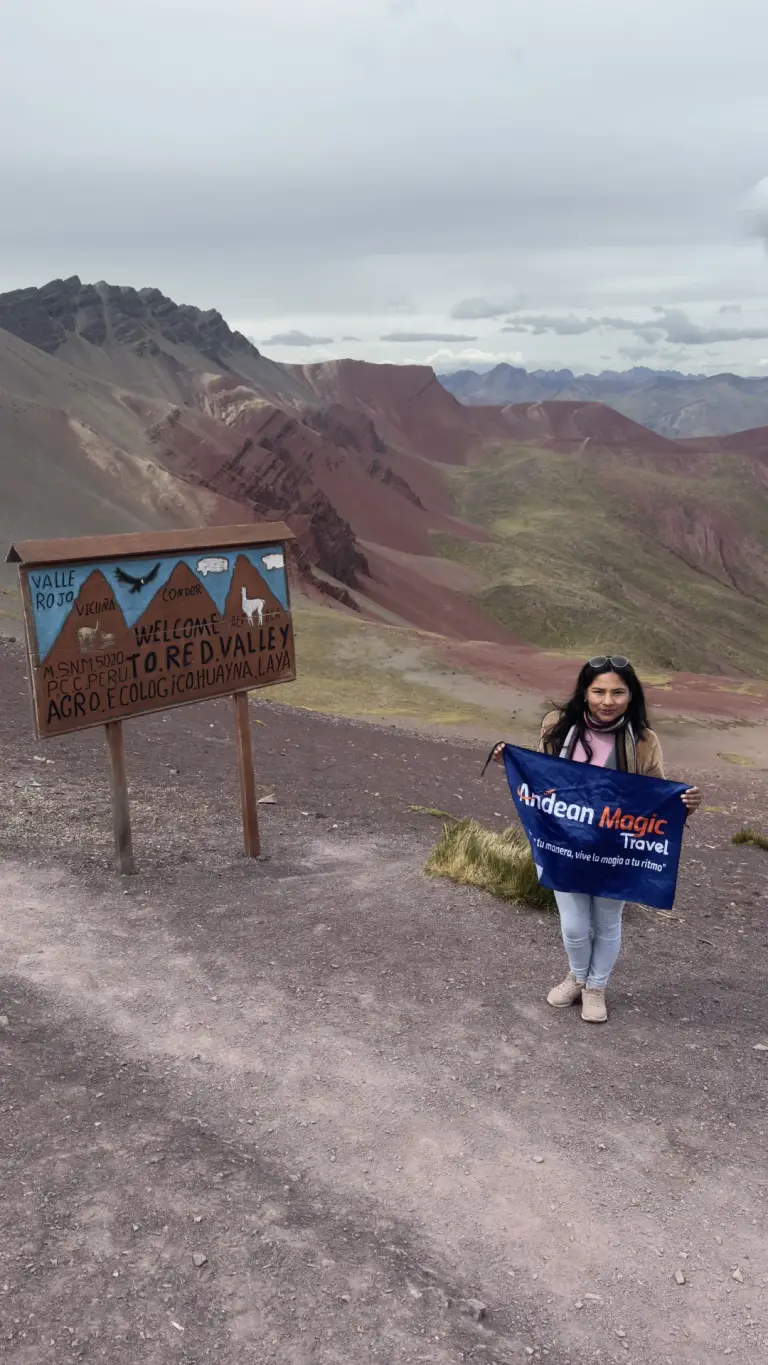 Viajera con la bandera de Andean Magic Travel junto al cartel de bienvenida al Valle Rojo